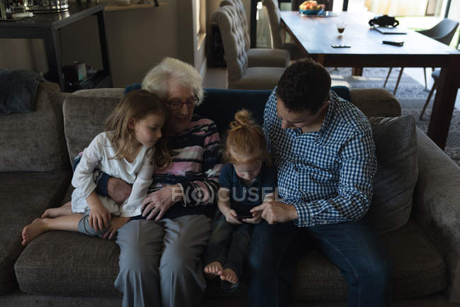 Familia multigeneración con teléfono móvil en el sofá en la sala de estar en casa - foto de stock
