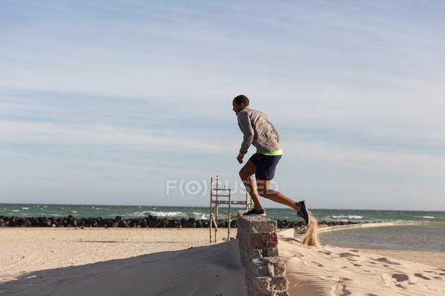 Athlète masculin faisant de l'exercice sur le mur voisin près de la plage — Photo de stock