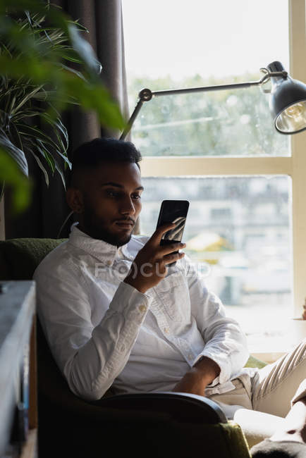 Man using mobile phone on arm chair in living room at home — Stock Photo
