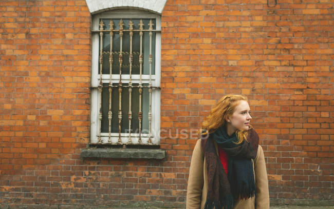 Рыжая женщина стоит с рукой в кармане против кирпичной стены — стоковое фото
