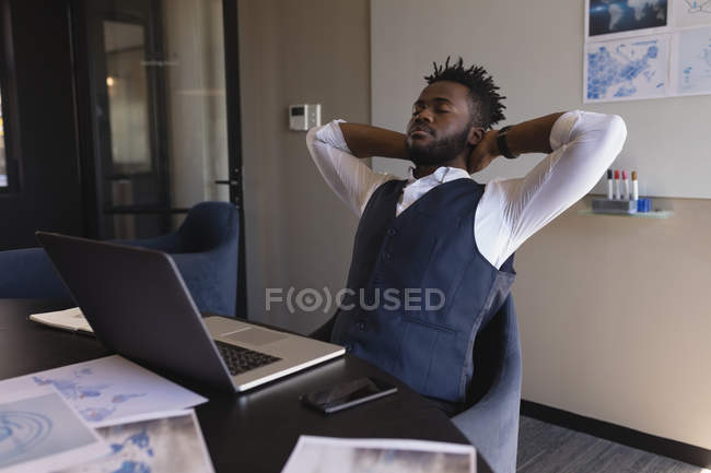 Businessman sitting with hands behind head in conference room at office — Stock Photo