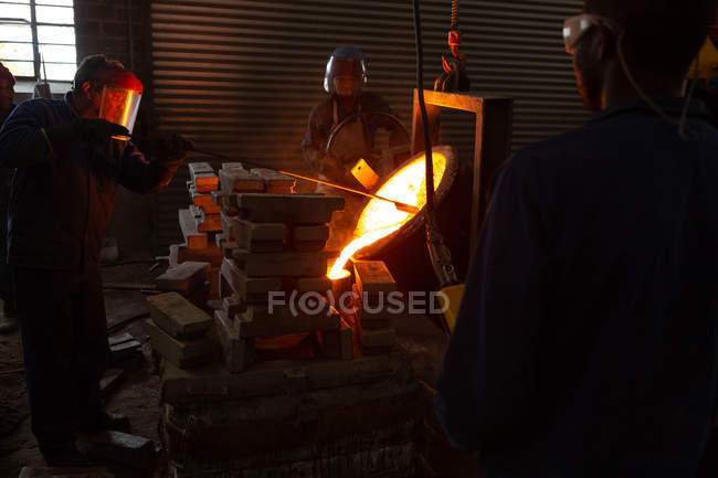 Workers pouring molten metal from flasks into moulds in foundry — Stock Photo