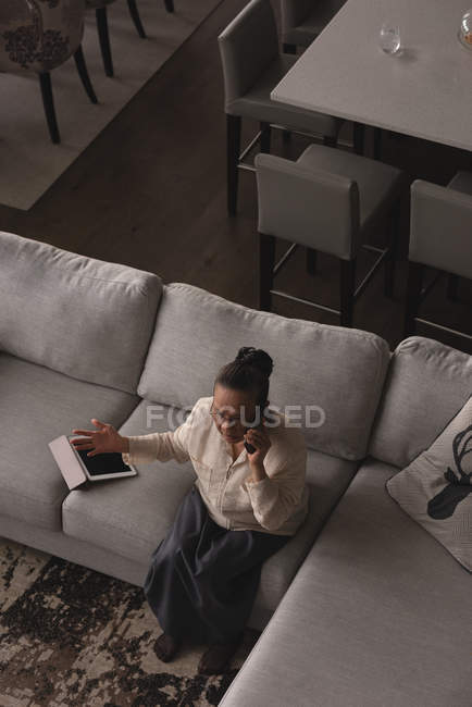 Senior woman talking on mobile phone on sofa in living room at home — Stock Photo