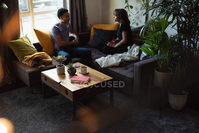 Couple interagissant les uns avec les autres tout en prenant un café sur le canapé dans le salon à la maison — Photo de stock
