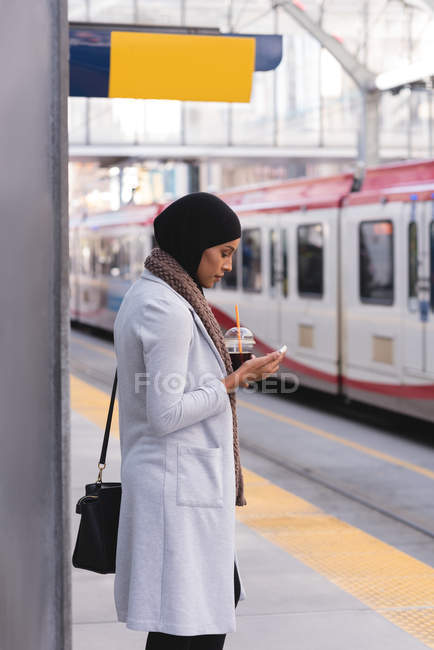 Hijab mujeres tomando café frío mientras usa el teléfono móvil en la ciudad - foto de stock