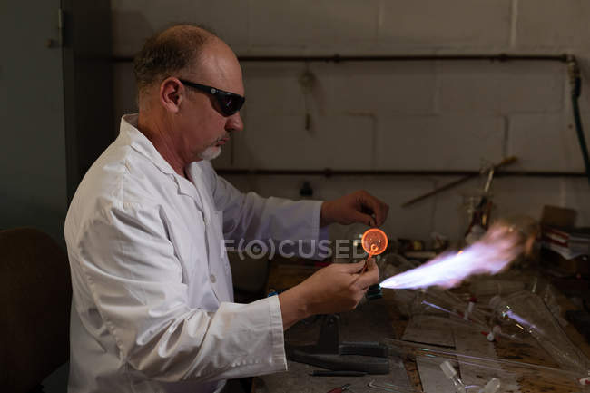 Вид збоку працівника чоловічої статі, що використовує зварювальний факел на скляній фабриці — стокове фото