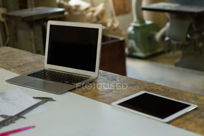 Ordenador portátil, tableta digital y pinza vernier en la mesa en taller de fundición - foto de stock