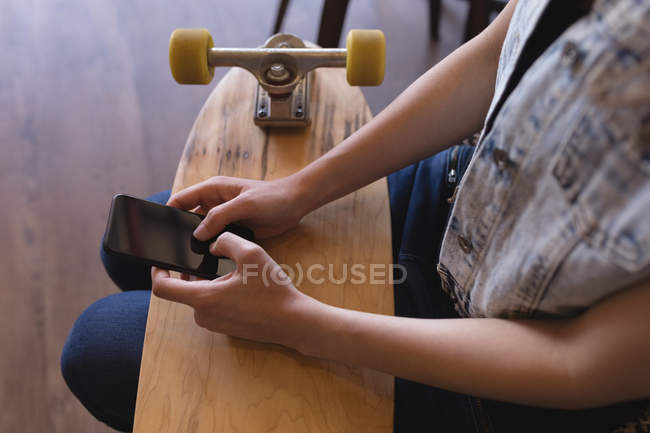 Средняя секция женщины исполнительной с помощью мобильного телефона со скейтбордом в офисе — стоковое фото