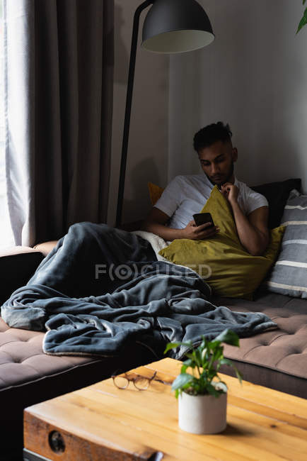 Человек, использующий мобильный телефон на диване в гостиной на дому — стоковое фото