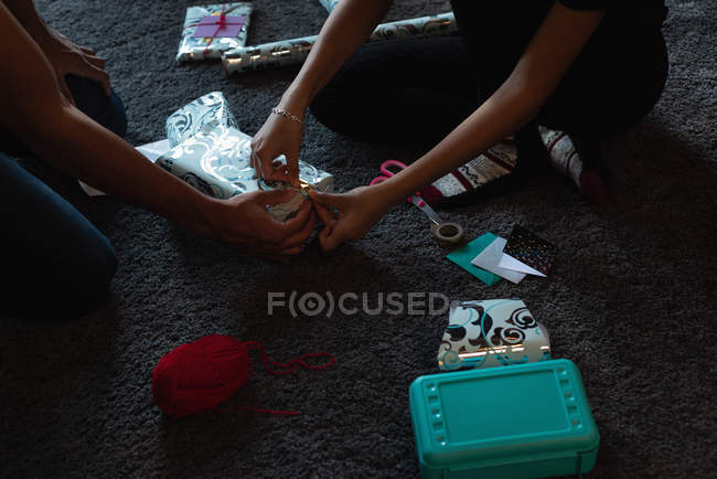Low section of couple wrapping gift box on floor at home — Stock Photo