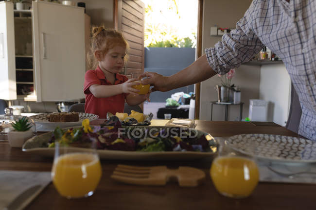 Батько подає апельсиновий сік дочці на обідній стіл вдома — стокове фото