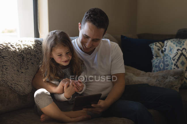 Padre e hija usando tableta digital en el sofá en la sala de estar en casa - foto de stock