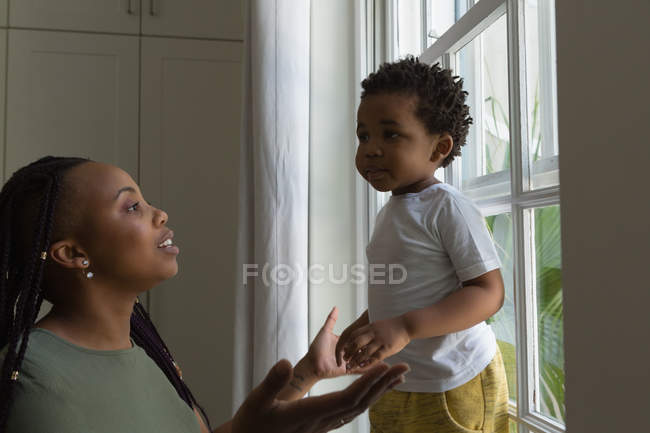 Madre jugando con su hijo cerca de la ventana en casa - foto de stock