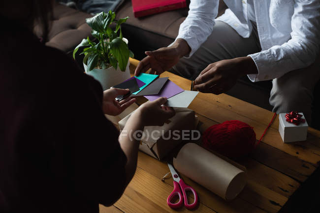 Sección media de la pareja eligiendo etiqueta de regalo en la sala de estar en casa - foto de stock