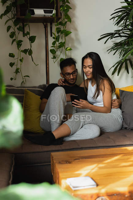 Пара с помощью мобильного телефона на диване в гостиной на дому — стоковое фото
