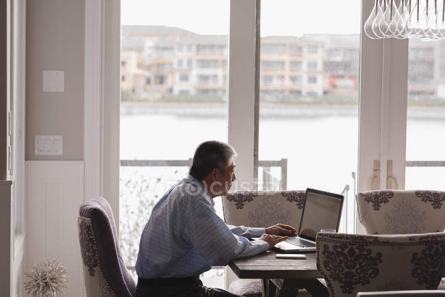 Side view of senior man using laptop at home — Stock Photo