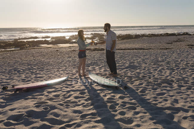 Seitenansicht von Paar beim Anstoßen auf Bierflasche am Strand — Stockfoto