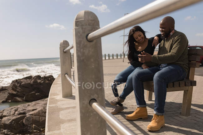 Happy couple discussing on mobile phone on promenade — Stock Photo
