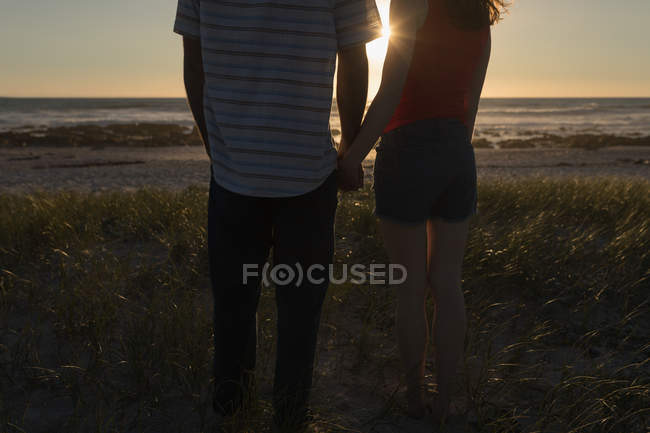 Section basse du couple tenant la main et debout sur la plage — Photo de stock