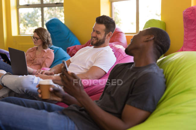 Business executives talking with each other while sitting on bean bag in office — Stock Photo