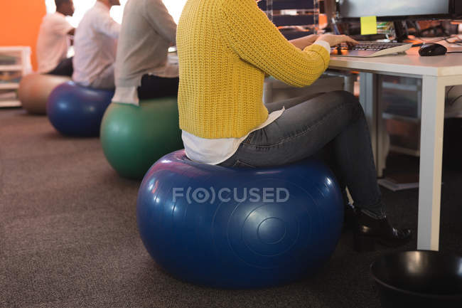 Executivos de negócios que trabalham na mesa enquanto estão sentados na bola de exercício no escritório — Fotografia de Stock