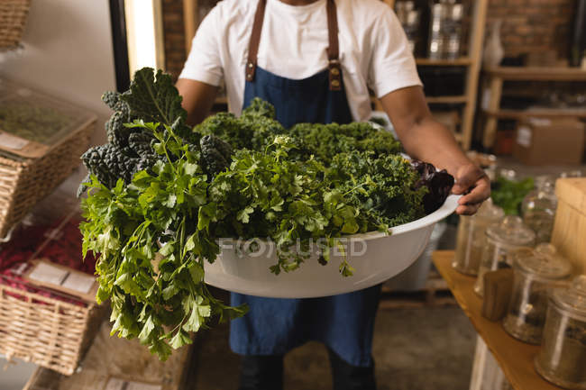 Male staff holding bathtub of green vegetables in supermarket — Stock Photo
