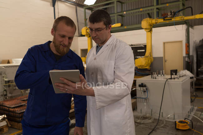 Ingenieros robóticos discutiendo sobre tableta digital en almacén - foto de stock