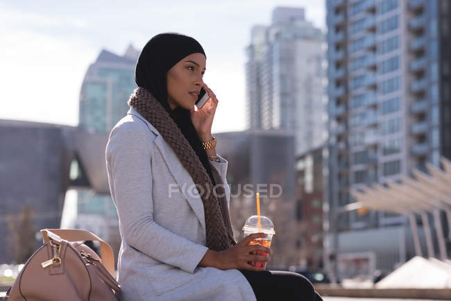 Hijab-Frau trinkt kalten Kaffee, während sie in der Stadt mit dem Handy telefoniert — Stockfoto
