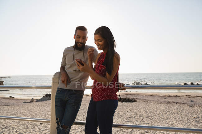 Pareja feliz usando el teléfono móvil en el paseo marítimo - foto de stock