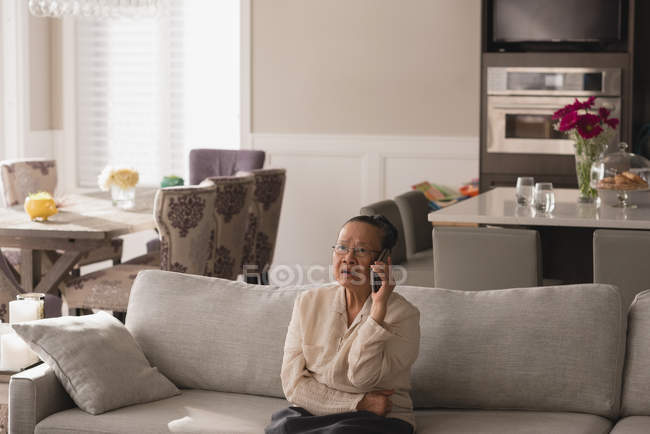 Mulher sênior conversando no telefone celular na sala de estar em casa — Fotografia de Stock