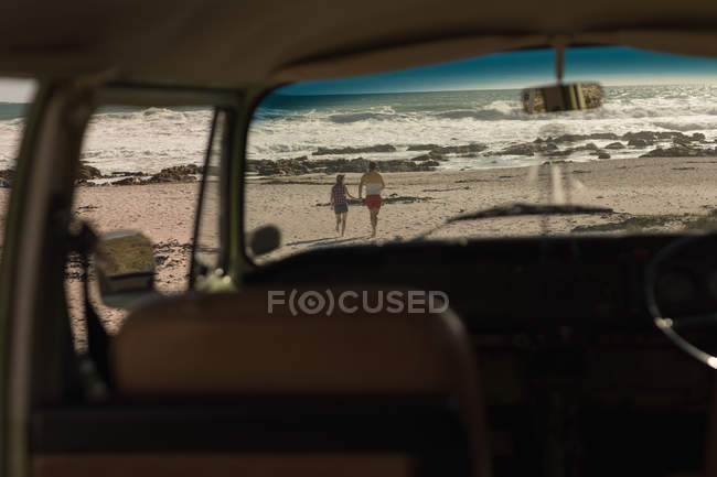 Вид сзади на пару, держащуюся за руки и бегающую по пляжу — стоковое фото