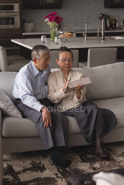Couple de personnes âgées discutant sur une tablette numérique sur le canapé dans le salon à la maison — Photo de stock