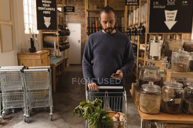 Hombre enfocado usando el teléfono móvil mientras compras en el supermercado - foto de stock