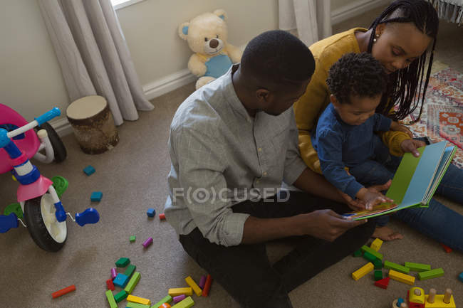 Родители читают книжку с картинками со своим сыном в гостиной дома — стоковое фото