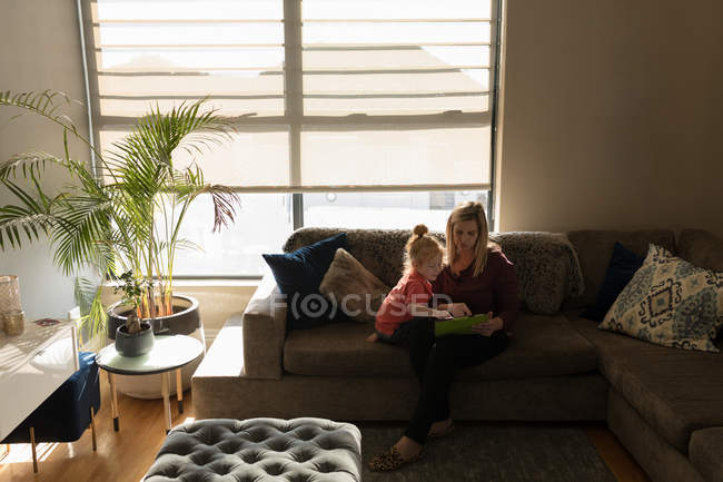 Мати і дочка використовують цифровий планшет на дивані у вітальні вдома — стокове фото
