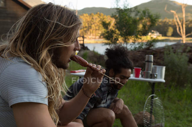 Молодий чоловік їсть ковбасу на території кемпінгу — стокове фото