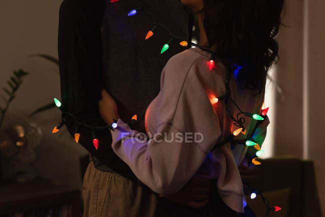 Casal romântico envolto em luzes de fadas abraçando uns aos outros em casa — Fotografia de Stock