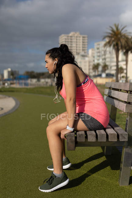 Вид сбоку женщины-бегуньи, сидящей на скамейке в парке — стоковое фото