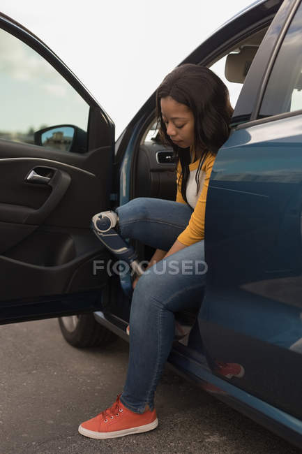 Side view of disabled woman tying shoelace while sitting in car — Stock Photo