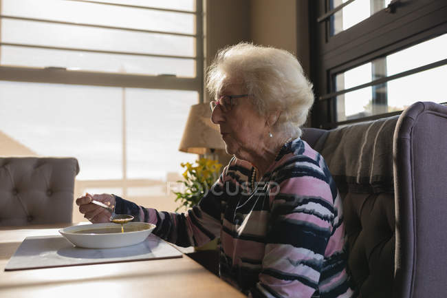 Vista lateral de la mujer mayor teniendo comida en casa - foto de stock