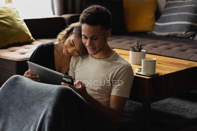 Пара с помощью мобильного телефона и цифрового планшета в гостиной на дому — стоковое фото