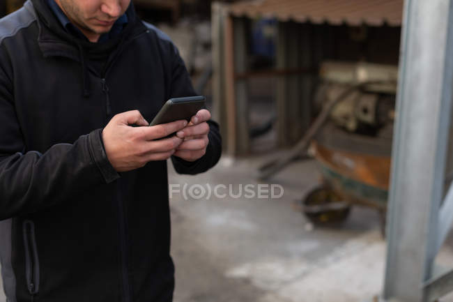 Partie médiane de l'homme utilisant le téléphone portable dans l'atelier de fonderie — Photo de stock