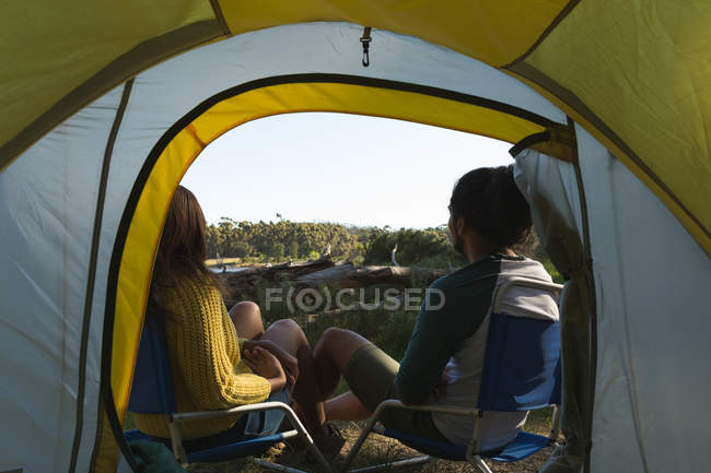 Вид сзади на пару, отдыхающую возле палатки в лесу — стоковое фото