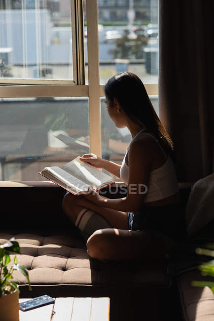 Donna che legge libro sul divano in soggiorno a casa — Foto stock