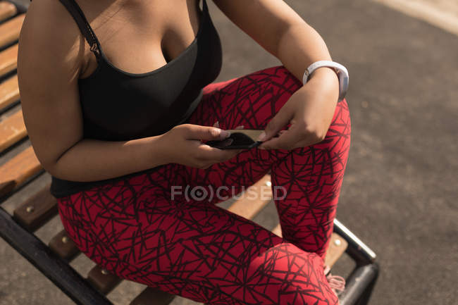 Partie médiane de la femme utilisant le téléphone mobile sur la chaise — Photo de stock