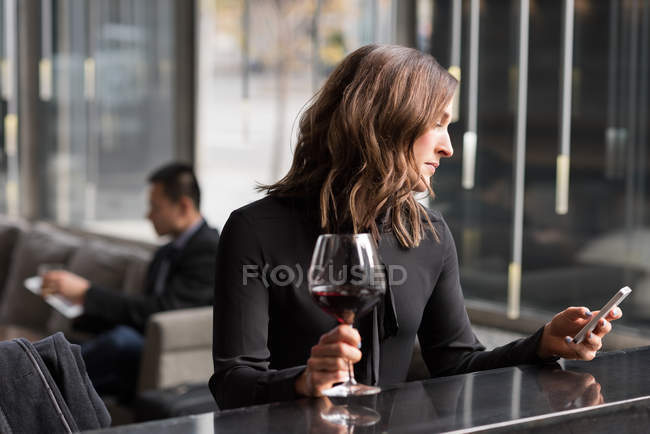 Деловая женщина с красным вином во время использования мобильного телефона в отеле — стоковое фото