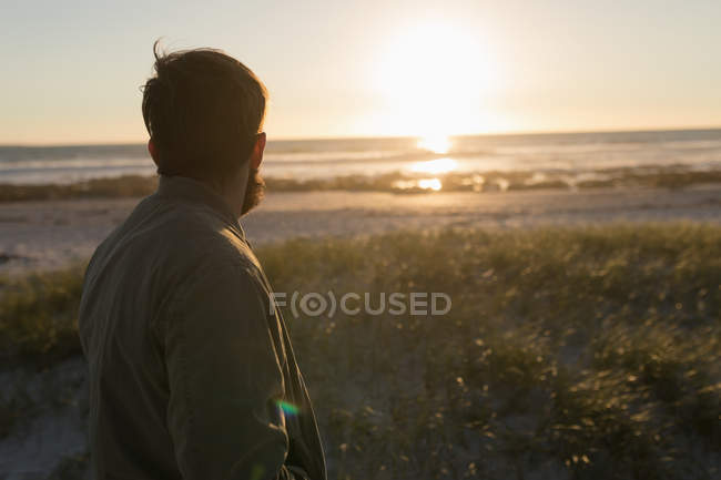 Вид ззаду чоловіка, що стоїть на пляжі під час заходу сонця — стокове фото