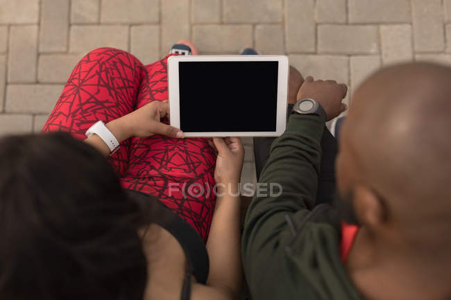 Frais généraux du couple utilisant la tablette numérique sur le banc de promenade — Photo de stock