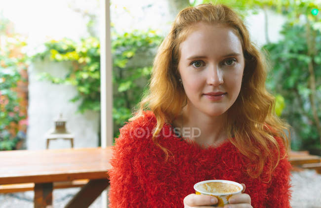 Рыжая женщина держит кофейную кружку в открытом кафе — стоковое фото