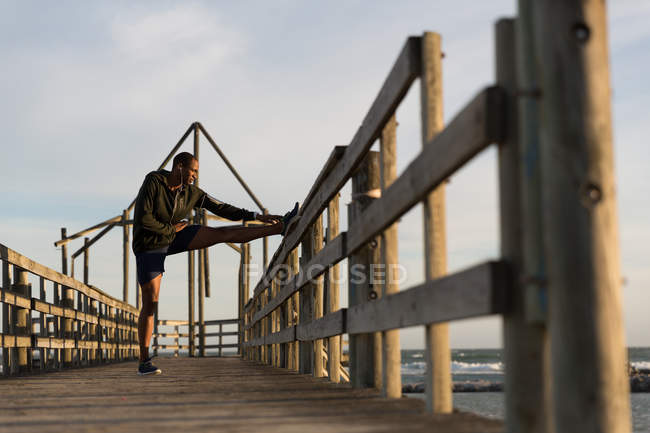 Male athlete stretching on pier at beach — Stock Photo